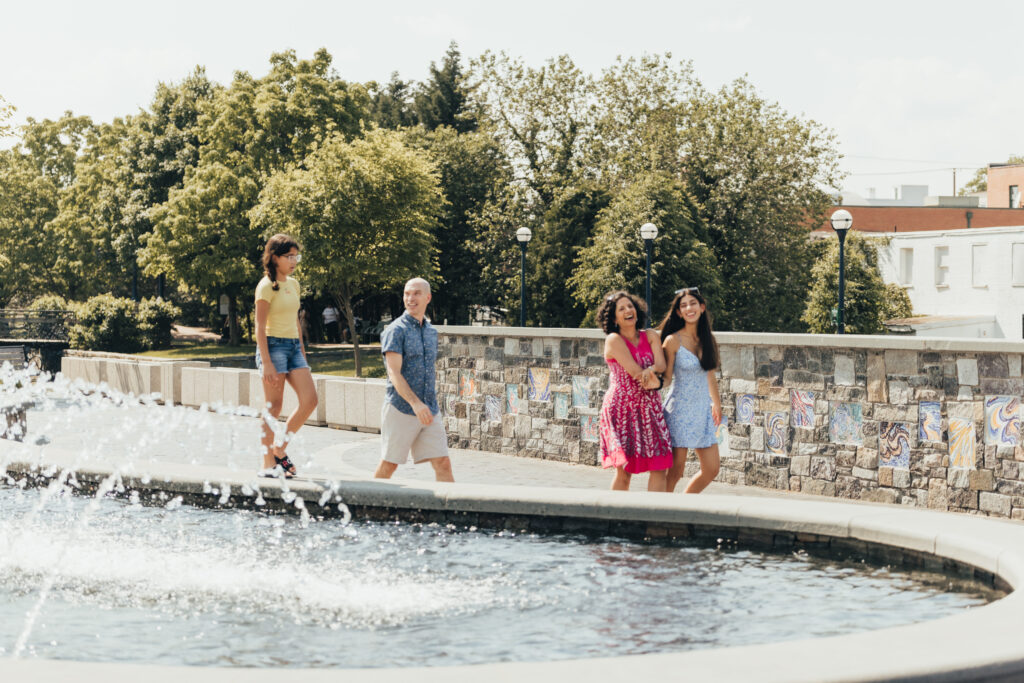 A family of four is walking on Carroll Creek along a water fountain.