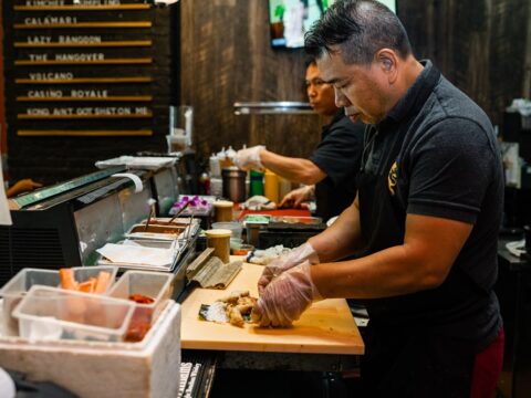 A man in a black shirt makes a sushi roll on a wooden block